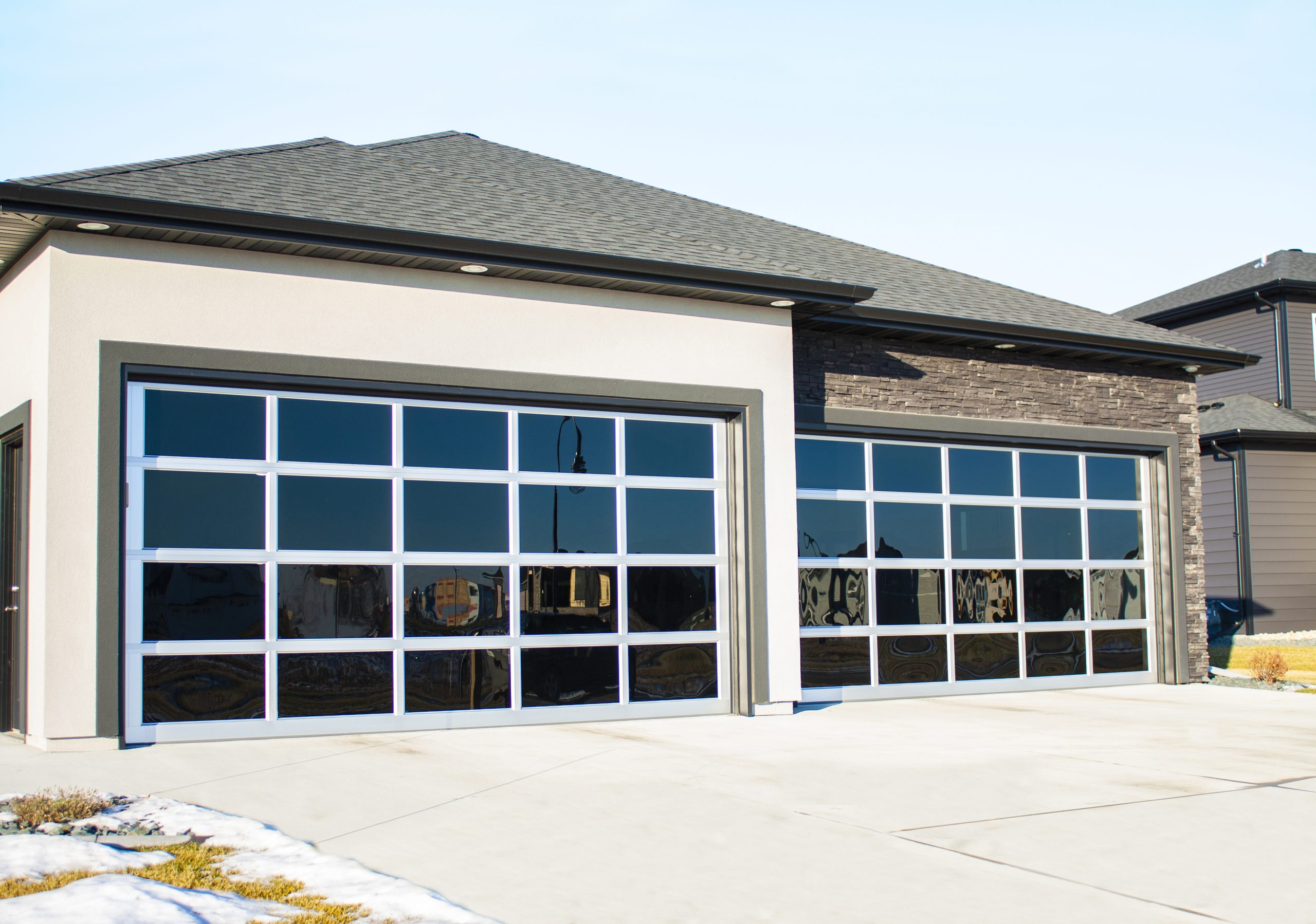 Modern residential garage with large glass-paneled doors, showcasing sleek architectural design, under a clear sky.