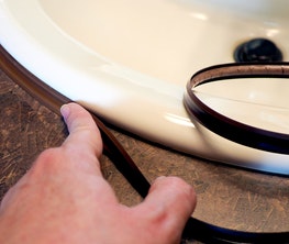 A hand applying flexible trim around the edge of a sink, demonstrating the use of BioPlastic Solutions' custom profile extrusion product.