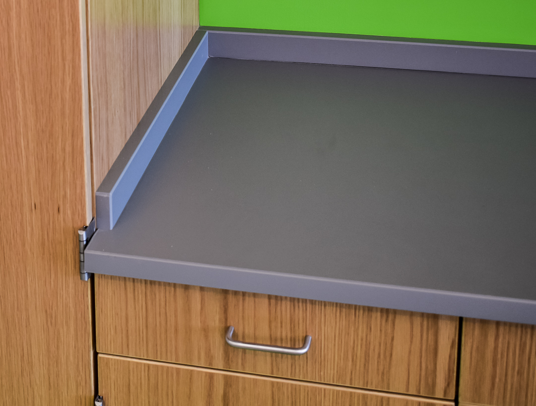 Gray countertop with a green wall background, featuring wooden cabinetry and a metal handle, illustrating modern design elements.