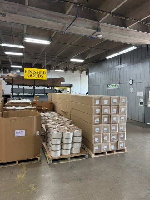 Warehouse interior with stacks of boxed and wrapped BioPlastic Solutions products labeled as "Finished Goods," ready for distribution.
