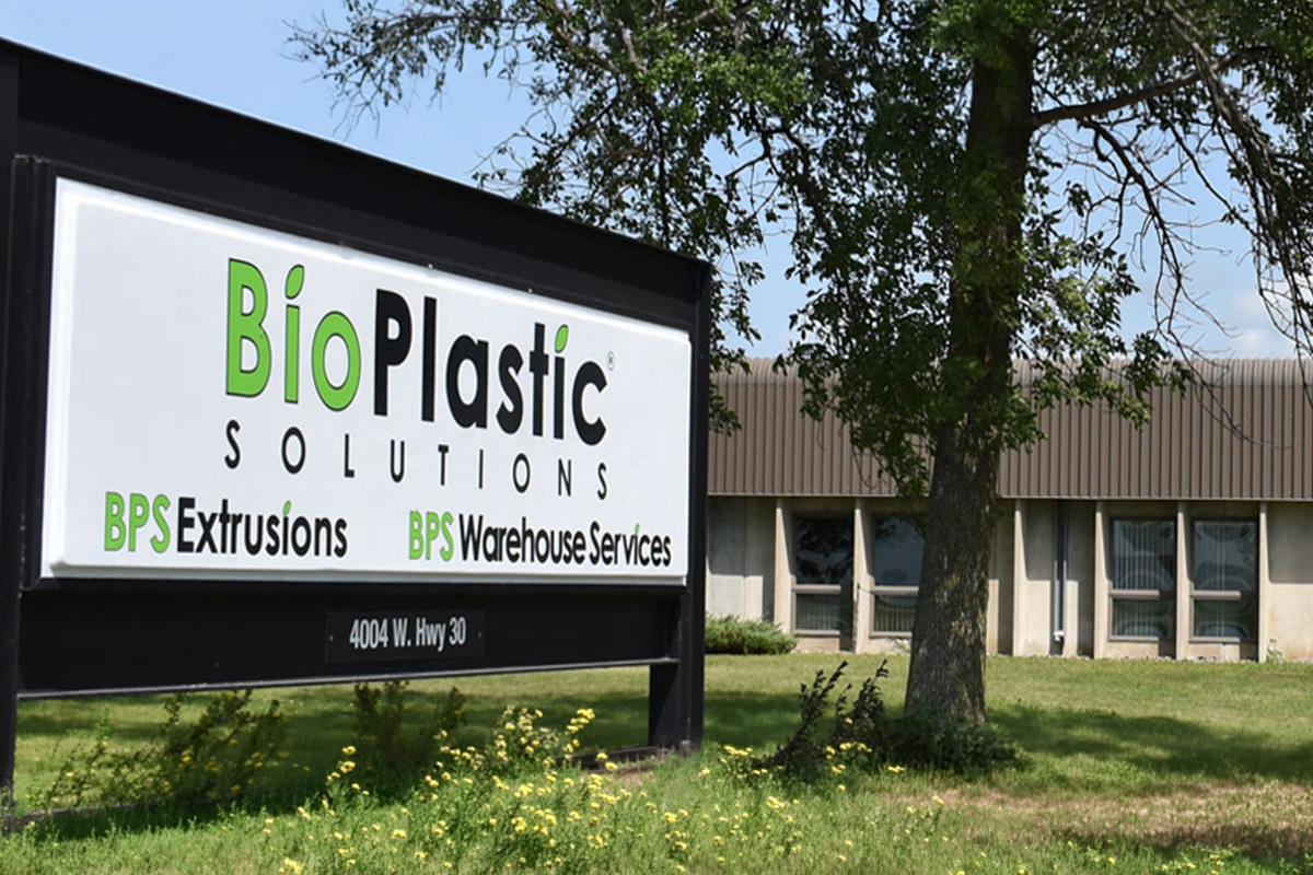 Sign for BioPlastic Solutions with text "BPS Extrusions" and "BPS Warehouse Services" in front of a building and tree.