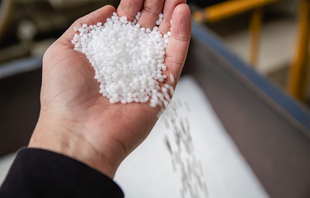 Hand holding a handful of white biodegradable resin pellets, symbolizing sustainable materials used in bioplastic extrusion.