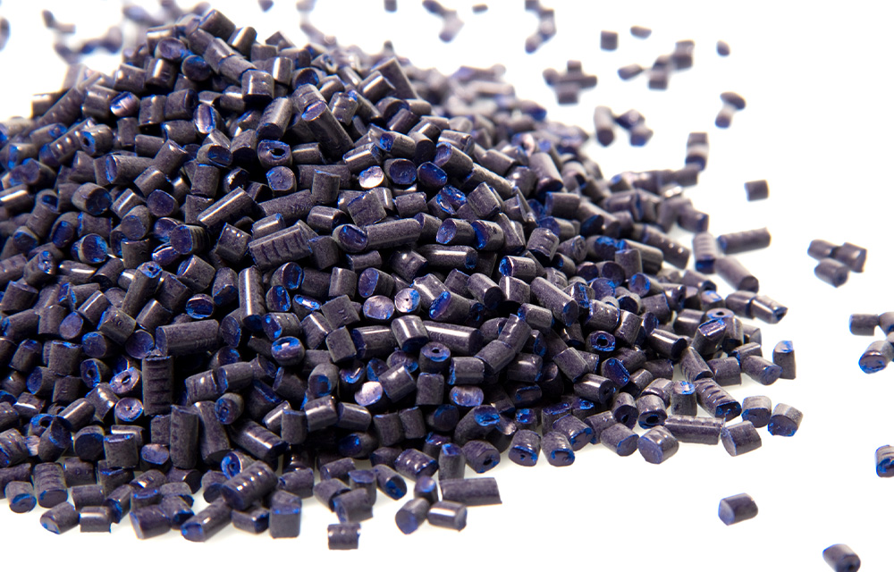 Pile of dark blue plastic pellets used in manufacturing, representing recycled content for sustainable bio-extrusion solutions.